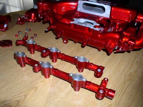 1996 Ford Probe - Red intake manifold and fuel rails are laid out on a wooden table, likely for installation or display.