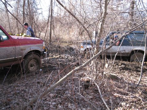 1995 Ford Bronco - Two SUVs are stuck in the mud and trees, with one person visible in each vehicle.
