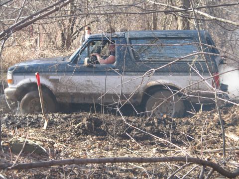 1995 Ford Bronco - A Ford Bronco is stuck deep in the mud, with a shovel nearby and a person in the driver's seat.