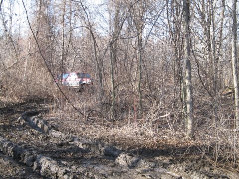 1995 Ford Bronco - A red and white SUV is stuck in the mud and trees, with visible tire tracks in the foreground.