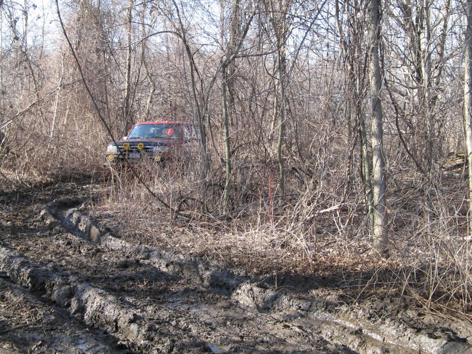 Red SUV with yellow fog lights stuck in muddy terrain surrounded by trees