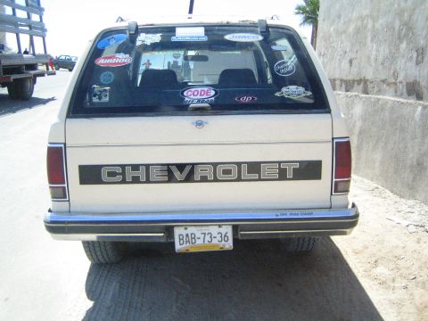 1990 Ford Bronco - tan rear tailgate of a Chevrolet SUV displays the CHEVROLET name and a sticker-covered rear window with a yellow Mexican license plate.