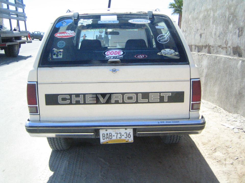 Rear of a tan Chevrolet SUV with sticker-covered window and Mexican plate