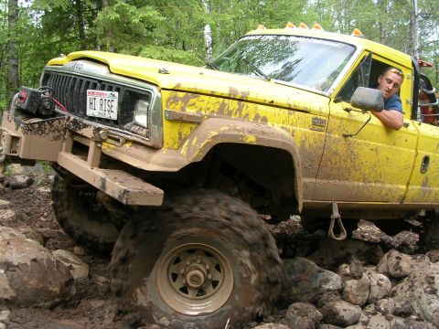 1986 Jeep J-10 - This yellow 1986 Jeep J-10 navigates a challenging off-road course, kicking up mud and dirt.