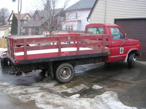 1986 Jeep J-10 - A red flatbed truck with wooden sides sits in a driveway with melting snow on the ground.
