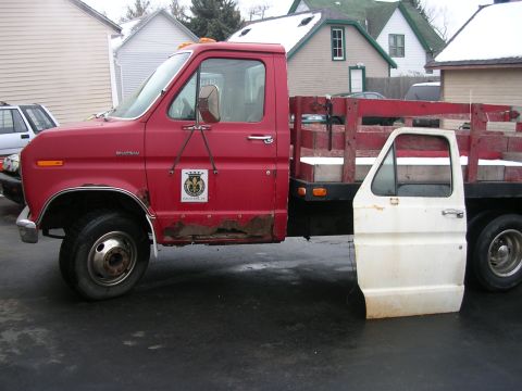 1986 Jeep J-10 - A red flatbed truck sits with its driver's side door removed and placed on the ground next to it.