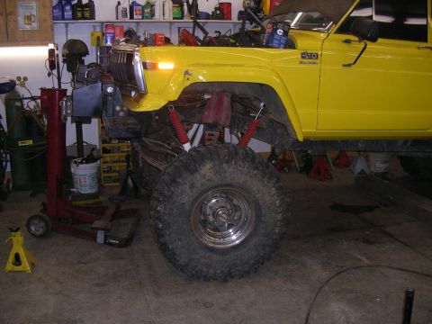 1986 Jeep J-10 - A yellow Jeep J-10 pickup truck is shown in a garage with its hood up and large tires. The vehicle appears to be undergoing maintenance or…