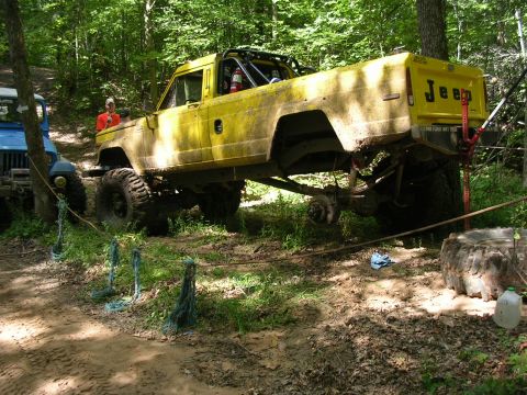 1986 Jeep J-10 - A yellow 1986 Jeep J-10 pickup truck with a roll cage is seen on an off-road trail next to a blue Jeep.