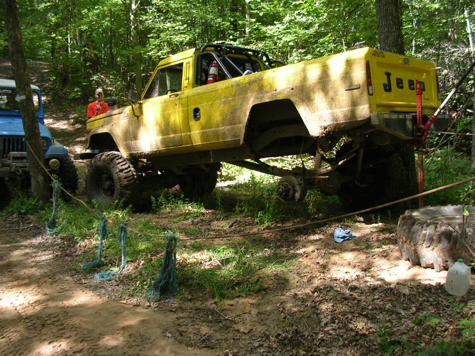 Yellow 1986 Jeep J-10 pickup truck with roll cage on off-road trail