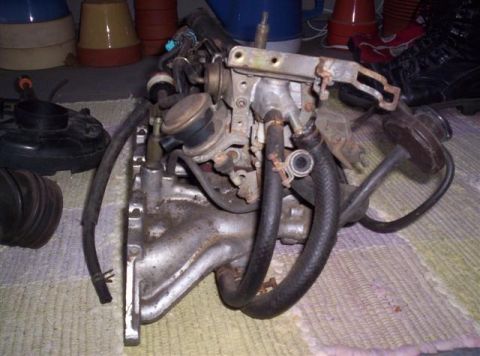 1987 Suzuki Samurai - A close-up view of an engine intake manifold assembly, likely a carburetor setup, with various hoses and metal components.