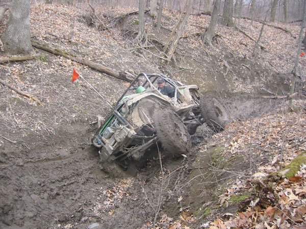 Off-road buggy stuck in a muddy ditch on a wooded trail
