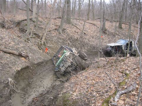 1992 Ford Bronco - Two off-road vehicles navigate a challenging muddy terrain in a forest setting.