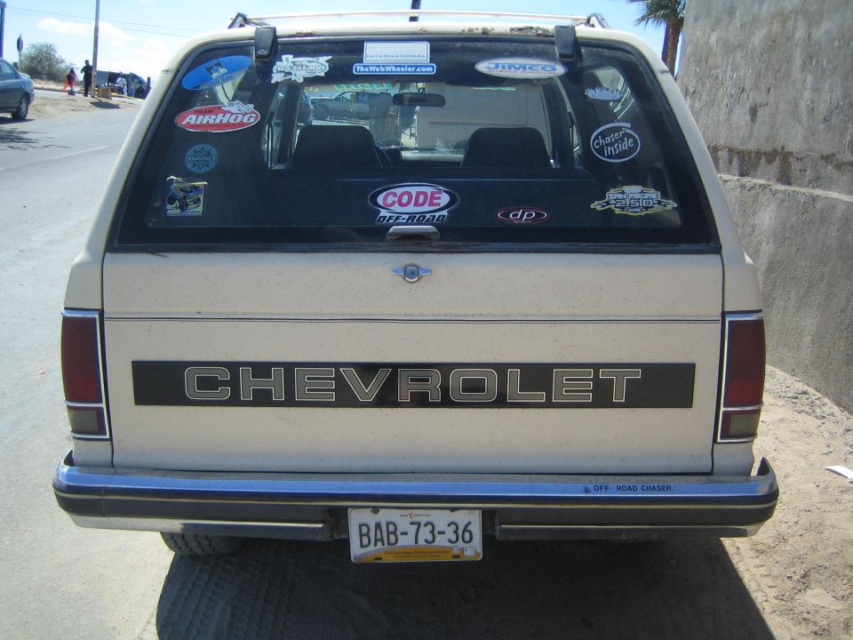 Rear of a tan Chevrolet SUV with sticker-covered rear window and yellow plate