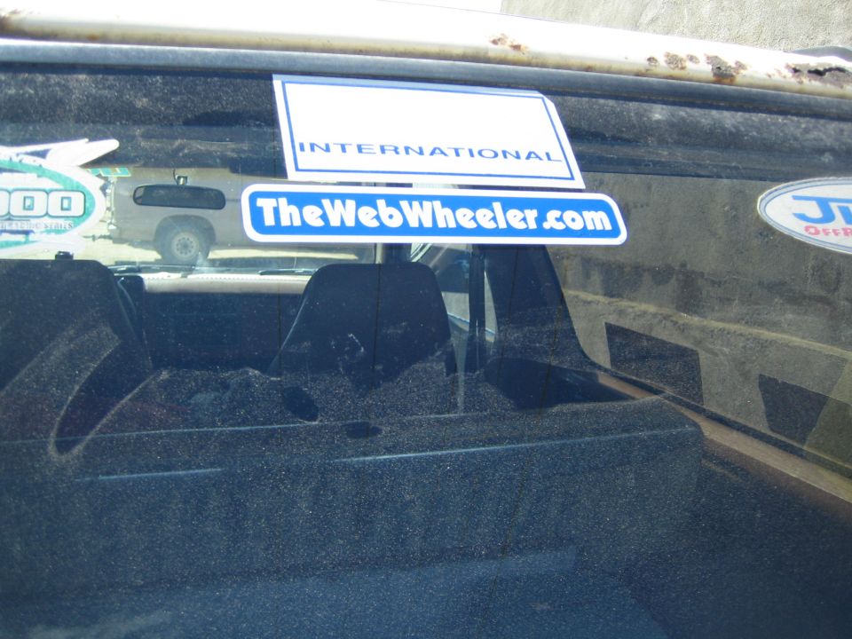 Close-up of TheWebWheeler.com and INTERNATIONAL stickers on a dusty rear window
