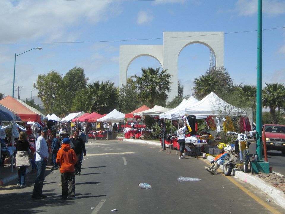 Street vendor market with white tents below twin white arches on a sunny day