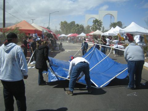 1990 Ford Bronco - group of people struggle with a collapsed blue tent amid scattered vendor stalls on a windy street near twin white arches.