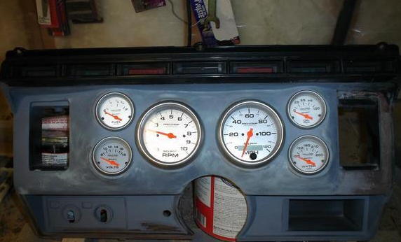 Custom dashboard assembly with fuel, volts, RPM, MPH, and water gauges. Some text visible on gauge labels and a can