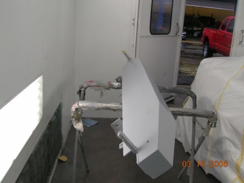 1985 Ford Bronco - A gray rear bumper is mounted on a stand inside a paint booth, with a red truck visible through an open door.