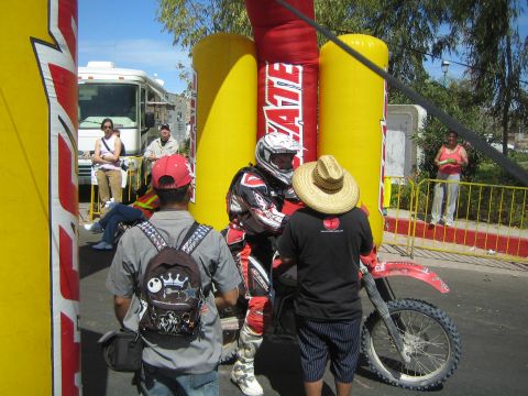 1990 Ford Bronco - Spectators and a helmeted rider gather around a red Honda dirt bike beneath a yellow and red inflatable Tecate arch.