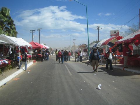 1990 Ford Bronco - dusty street lined on both sides with white and red vendor tents, with people walking and a Tecate sign in the distance.