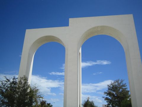 1990 Ford Bronco - Two tall white concrete arch structures rise against a blue sky over treetops, viewed from below.