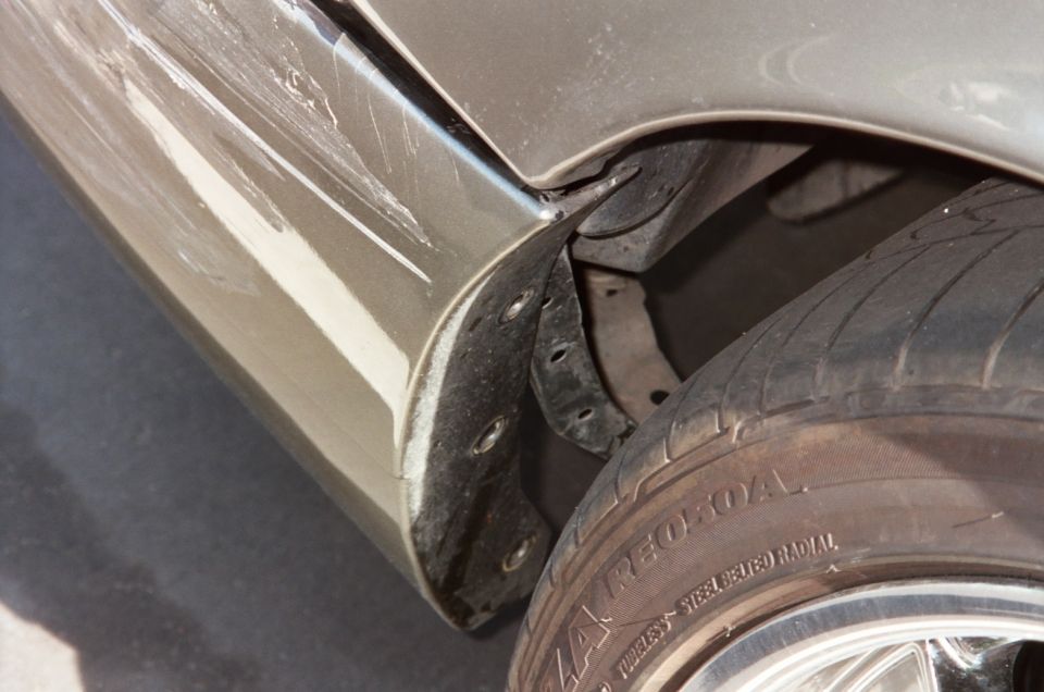 Close-up of a car's rear fender with significant scratches and damage, showing the wheel well and tire