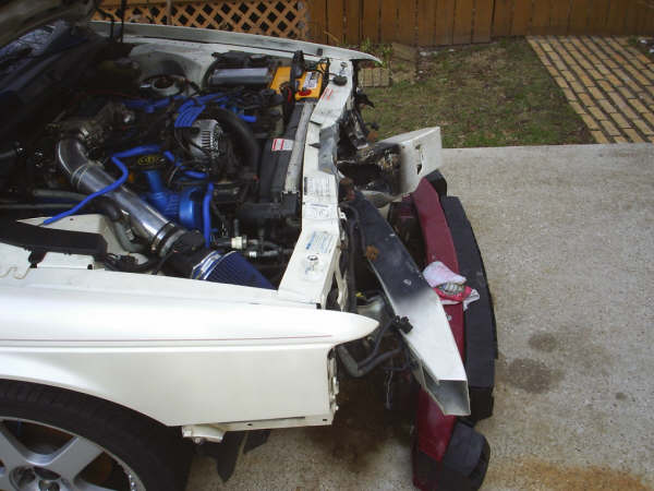 1996 Ford Thunderbird engine bay with aftermarket intake, front end damaged, parts piled up