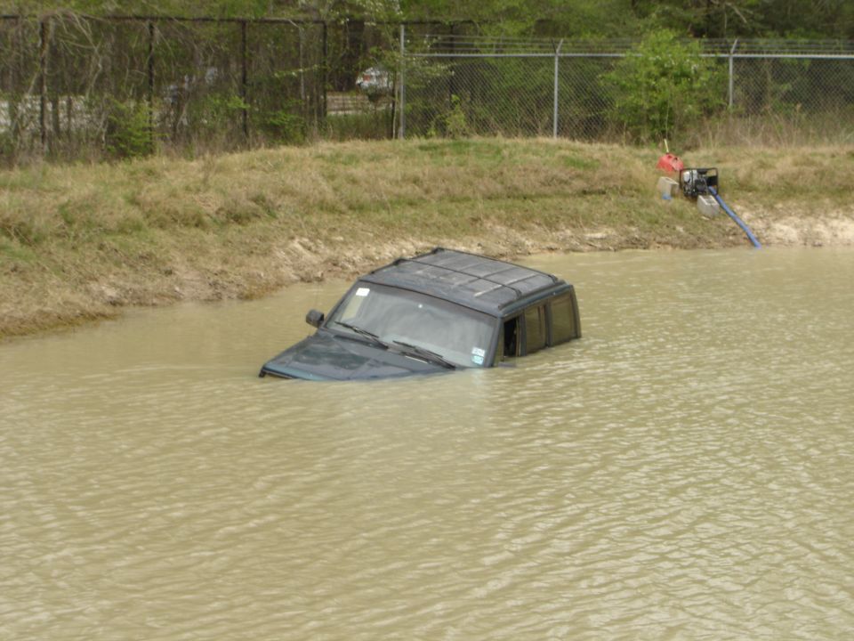 Dark SUV partially submerged in muddy water, front end lower than rear