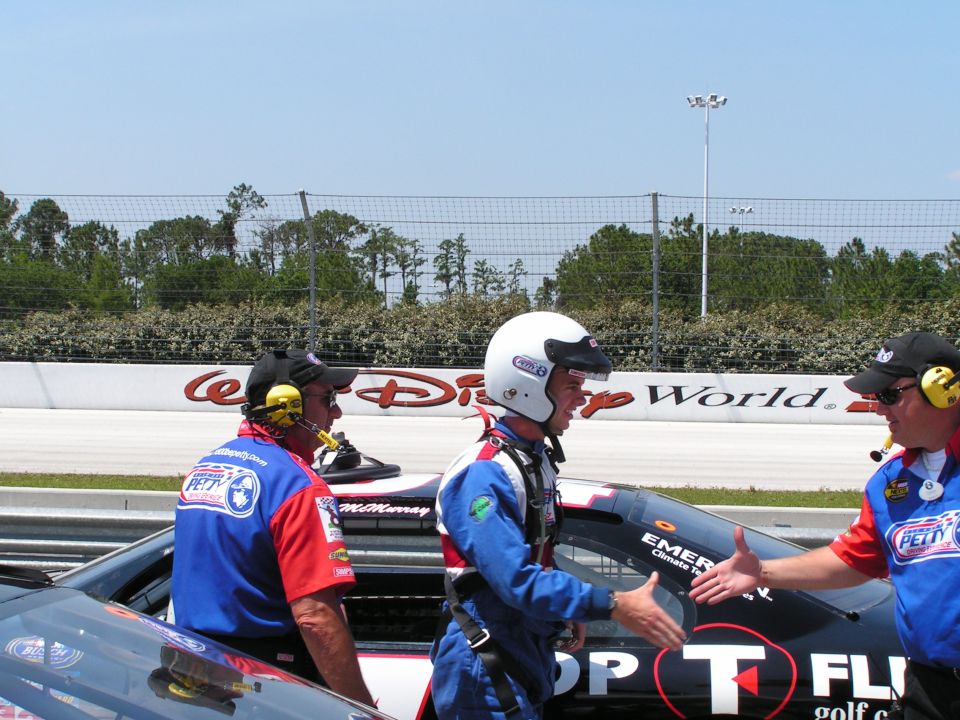 Richard Petty Driving Experience crew and helmeted driver beside black stock car at Disney track