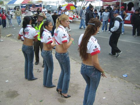 1990 Ford Bronco - People in tied red-and-white promotional shirts mingle in an outdoor event crowd, with a cameraman and vendor tents in the background.