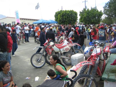 1990 Ford Bronco - Spectators and riders gather around a row of red Honda dirt bikes parked on a street, with a checkered flag flying overhead.