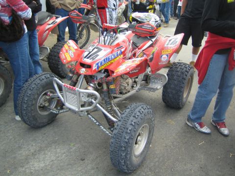 1990 Ford Bronco - red Honda four-wheeler ATV with Temecula Motorsports racing graphics and number 14 sits among onlookers' legs.