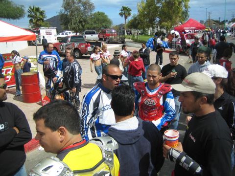 1990 Ford Bronco - dense crowd of off-road riders and spectators mingles on a street lined with pickups and tents at a desert race.