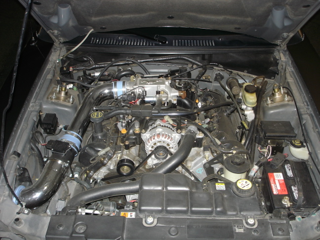 Engine bay of a Mustang with V8, alternator, intake, and battery visible