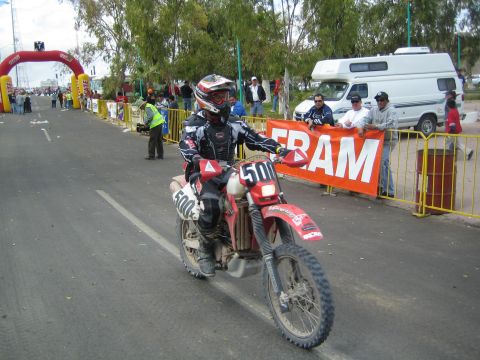 1990 Ford Bronco - racer on a red dirt bike numbered 500 rides past spectators and an orange Fram banner near a finish arch.