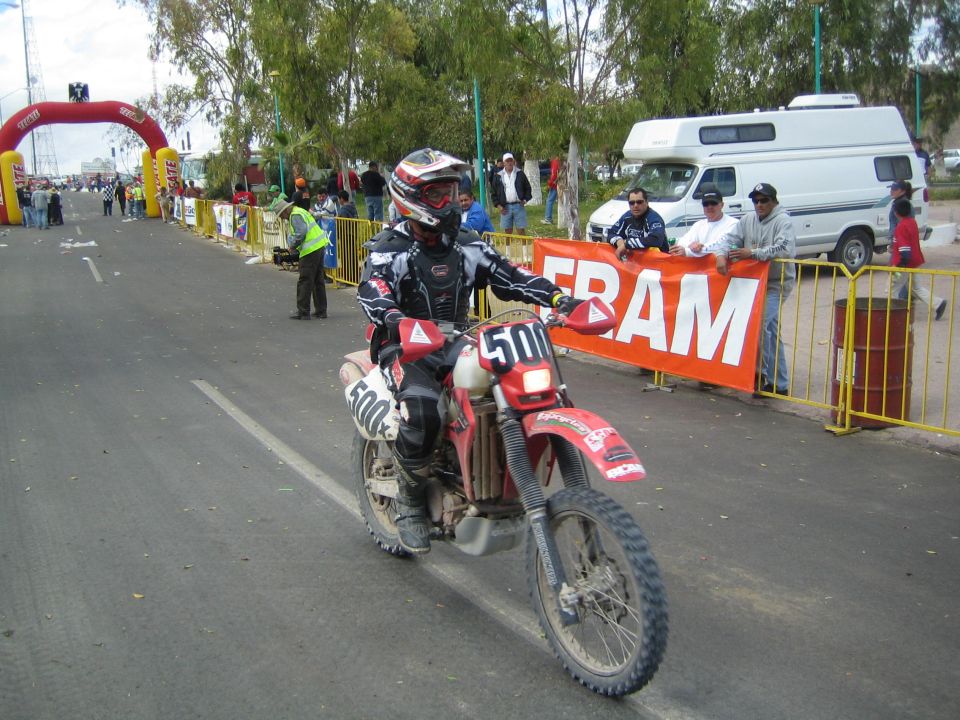 Rider on red dirt bike number 500 passing a Fram banner near a finish arch
