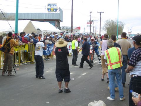 1990 Ford Bronco - Spectators line a barricaded street under a Corona Extra sign as a dirt-bike racer approaches the finish area.