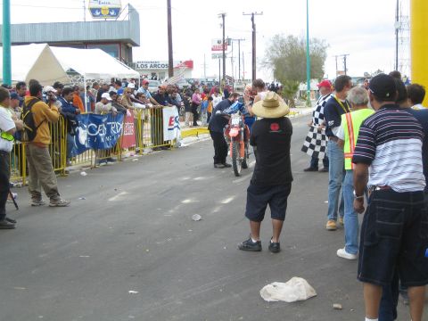 1990 Ford Bronco - photographer in a sombrero crouches to shoot an approaching dirt-bike racer on a crowd-lined finish street.
