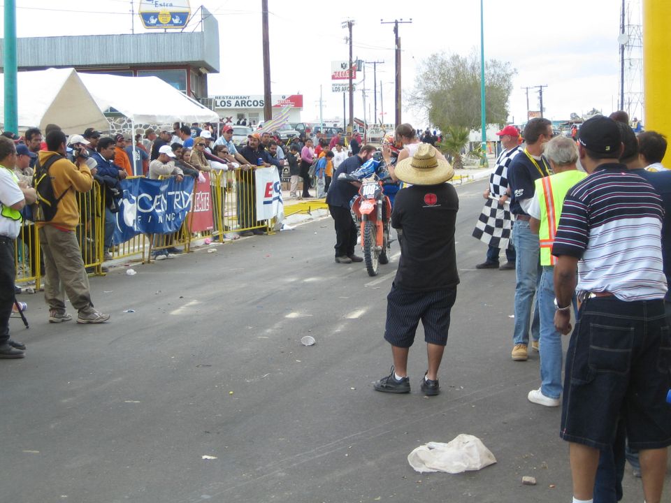 Photographer in a sombrero shoots a dirt-bike racer on a barricaded street