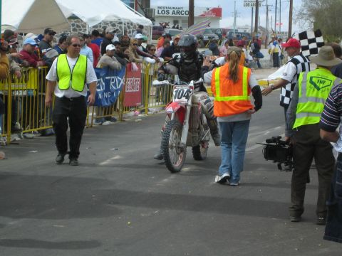 1990 Ford Bronco - rider on a red Honda dirt bike numbered 104 is met by officials in safety vests at the race finish line.