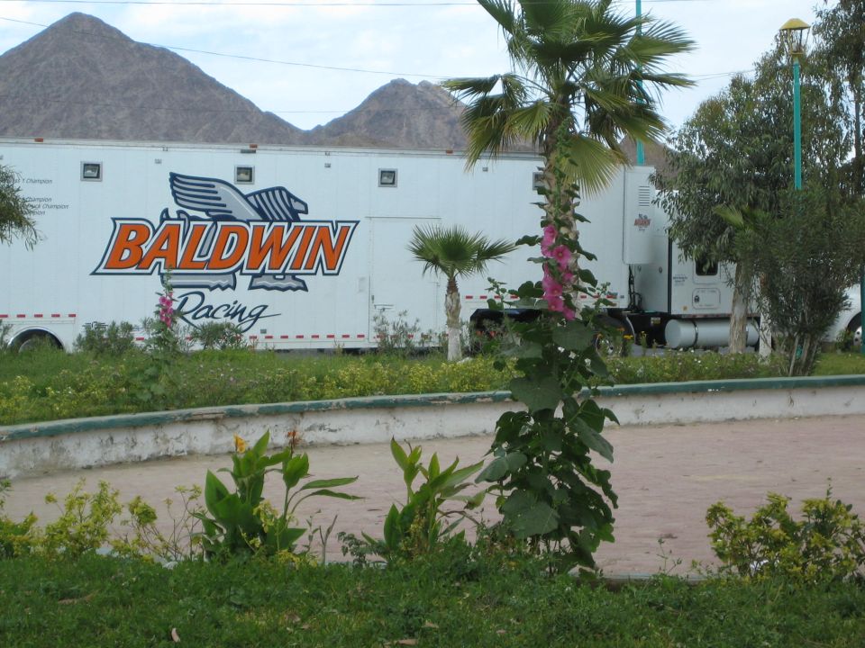 White Baldwin Racing semi-trailer parked behind a planter with mountains beyond
