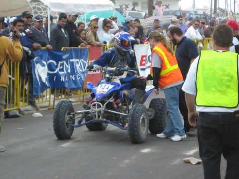 1990 Ford Bronco - racer on a blue ATV quad numbered 14a is met by officials in safety vests amid a crowded race finish.