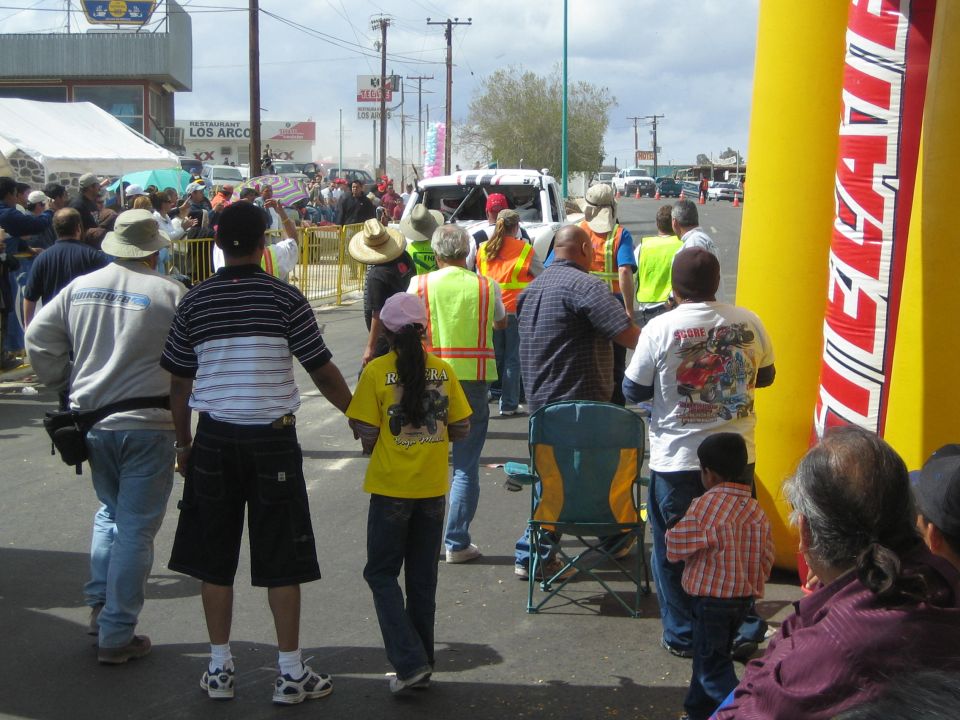 Crowd seen from behind watching a barricaded race street near a Tecate banner