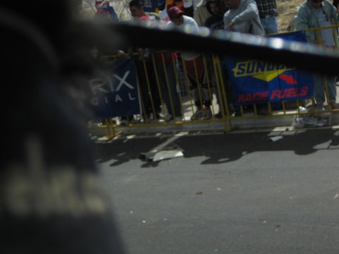 1990 Ford Bronco - dark blurred figure fills the foreground while a Sunoco Race Fuels banner hangs on barricades across the road.