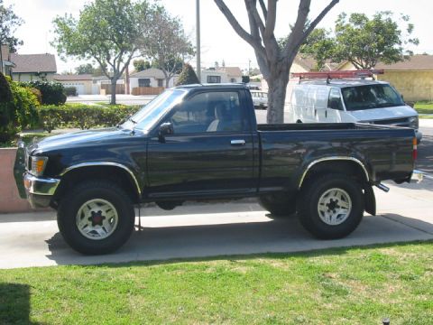 1989 Mazda MX-6 - A black pickup truck is parked on a driveway in front of a residential house, with a white van visible behind it.