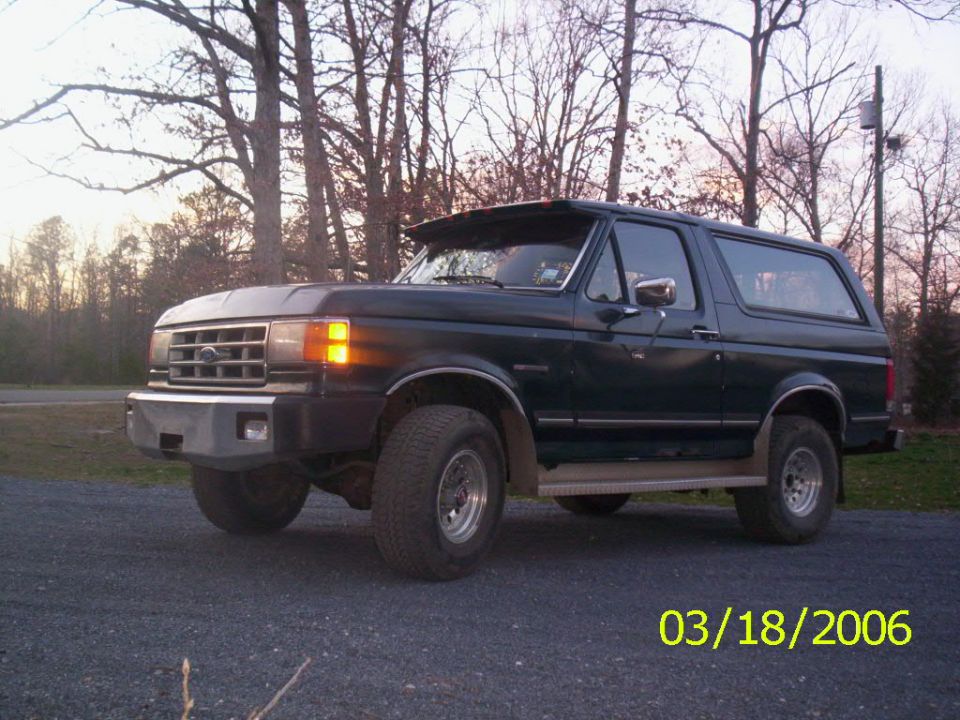 Dark green Ford Bronco with aftermarket bumper and sun visor parked on gravel. Date stamp reads 03/18/2006