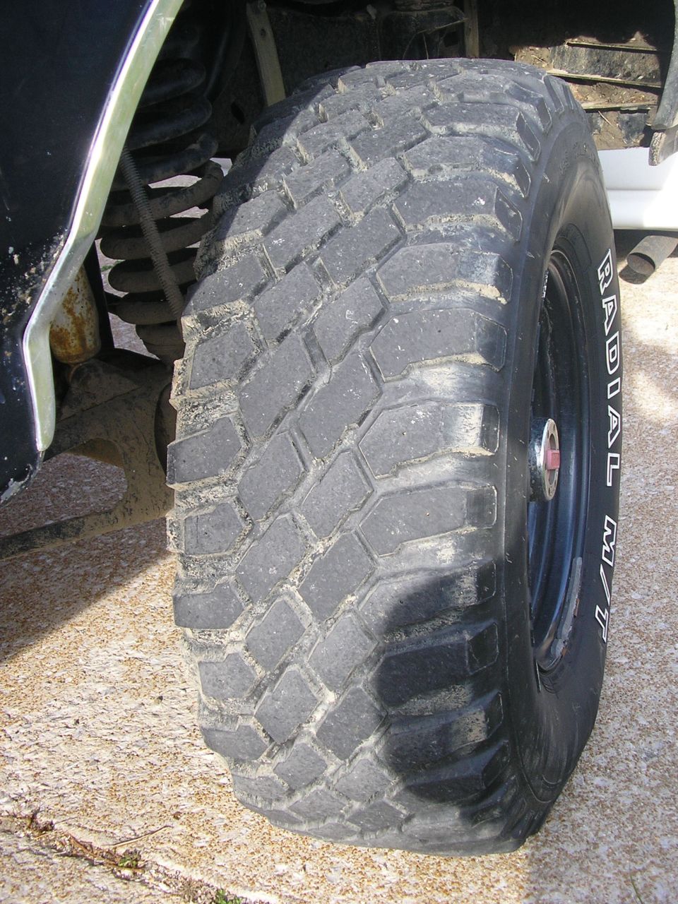 Mud-terrain tire on a black steel wheel, sidewall reads RADIAL M/T, on concrete