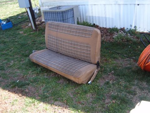 1988 Ford Bronco - Bench seat with tan and brown plaid upholstery is placed on the grass outdoors.