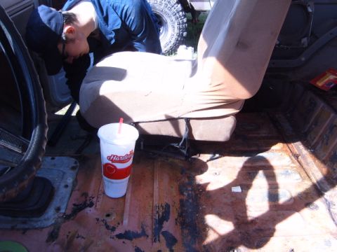 1988 Ford Bronco - A person works on the interior of a vehicle, with a drink and a tire visible.