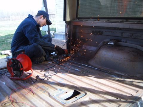 1988 Ford Bronco - A person uses an angle grinder to work on the metal bed of a pickup truck.